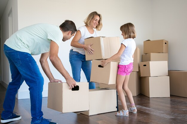 Gelukkige moeder, vader en kind houden kartonnen dozen en verhuizen naar een nieuw huis of appartement