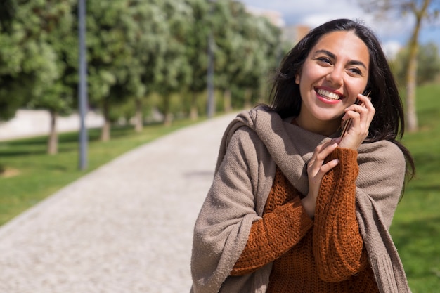 Gelukkige mooie dame die op telefoon in stadspark spreekt