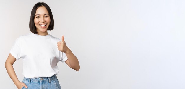 Gelukkige mooie Koreaanse vrouw die lacht, blij met duimen omhoog in goedkeuring die merk of com aanbeveelt