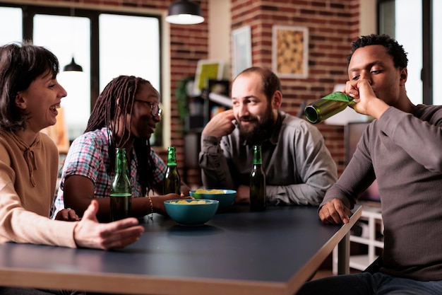 Gratis foto gelukkige multiraciale vrienden die thuis in de woonkamer zitten terwijl ze praten en genieten van snacks en drankjes. vrolijke jonge volwassenen die een gesprek hebben terwijl ze ontspannen met een positieve levensstijl.