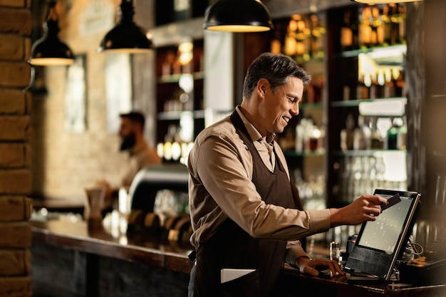 Gelukkige ober die kassa gebruikt terwijl hij bestellingen controleert en in een pub werkt