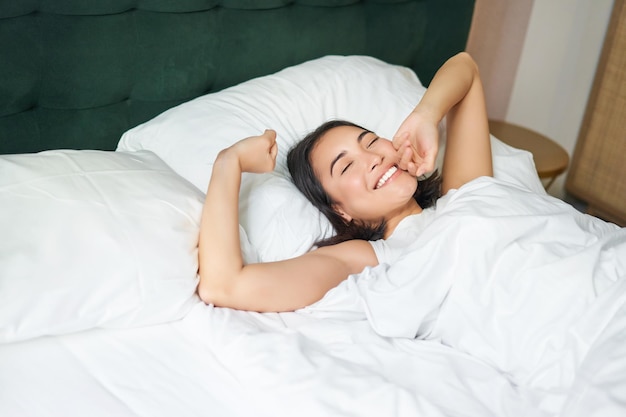 Gelukkige ochtenden mooi aziatisch meisje wordt wakker in een hotelkostuum dat in een wit bed ligt en haar armen strekt