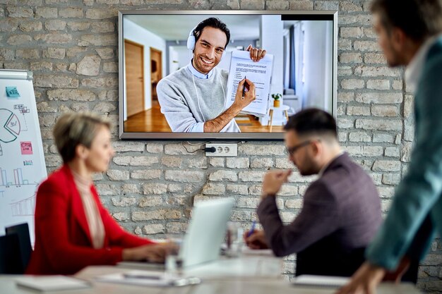 Gelukkige ondernemer die deelneemt aan een zakelijke bijeenkomst via videoconferentiegesprek en met zijn collega's over papierwerk praat