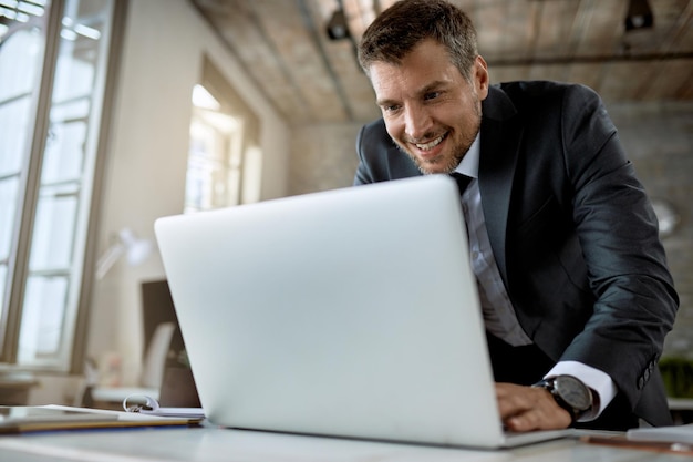 Gelukkige ondernemer die een e-mail typt terwijl hij op een laptop op kantoor werkt