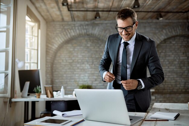 Gelukkige ondernemer leest iets op een computer terwijl hij aan zijn bureau staat