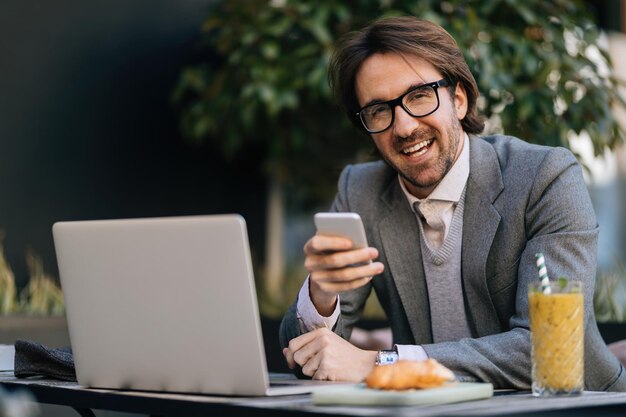 Gelukkige ondernemer sms't op mobiele telefoon terwijl hij tijdens een pauze op het terras zit