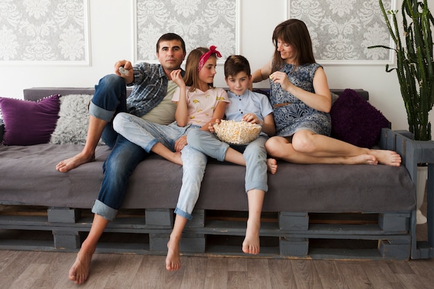 Gelukkige ouder met hun kinderen die op bank zitten en popcorn eten