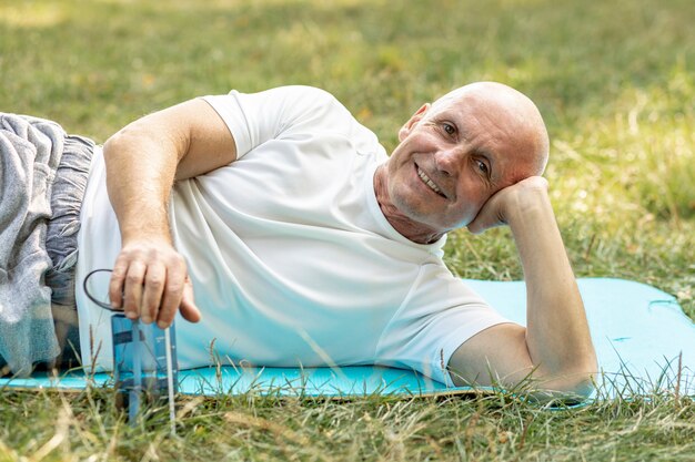 Gelukkige oudere mens die op yogamat rusten op gras