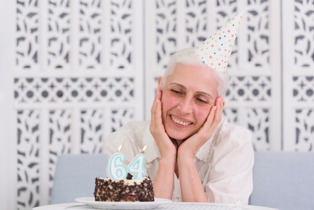 Gratis foto gelukkige oudere vrouw die smakelijke cake met gloeiende kaarsen op lijst bekijkt