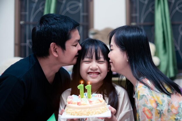 Gelukkige ouders die hun dochter kussen terwijl ze thuis een verjaardagskaars uitblazen