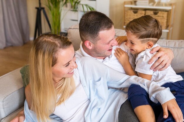 Gelukkige ouders die hun zoon houden en in woonkamer zitten