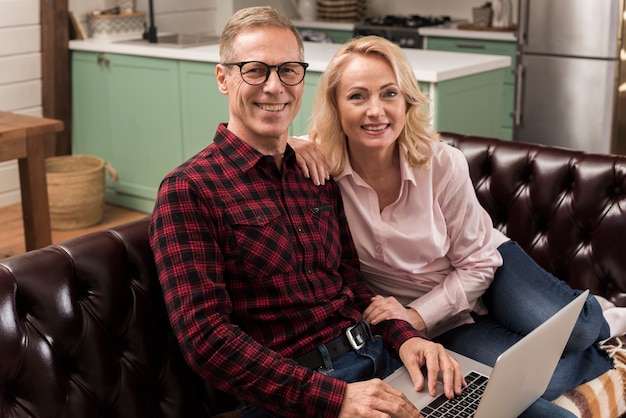 Gratis foto gelukkige ouders die met laptop op bank stellen