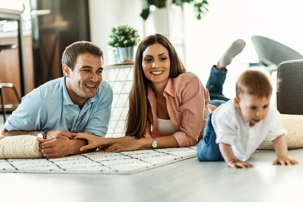 Gelukkige ouders genieten terwijl ze kijken hoe hun babyjongen op de vloer in de woonkamer kruipt