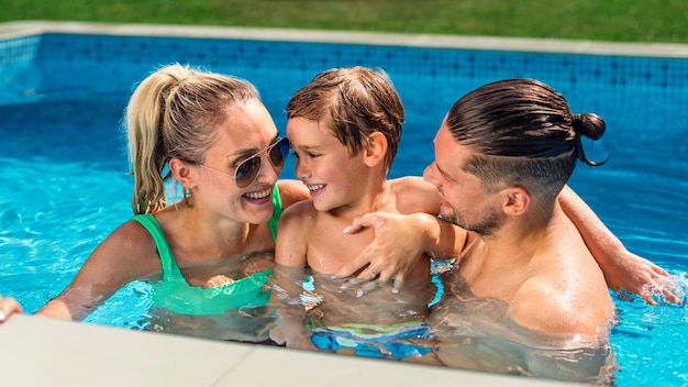 Gratis foto gelukkige ouders houden hun lachende zoon vast tijdens het zwemmen in het zwembad