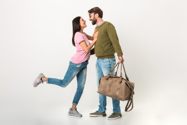 Gelukkige paar geïsoleerde, mooie lachende vrouw in roze t-shirt ontmoeting man in sweatshirt met reistas na een reis, gekleed in spijkerbroek, romantische liefde