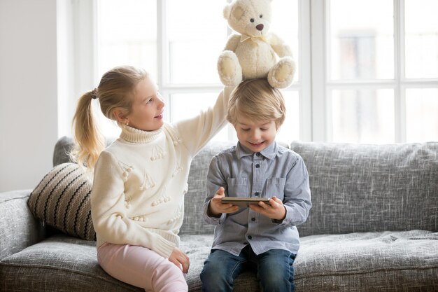 Gelukkige peuterjongen die tablet gebruiken terwijl zuster het spelen met stuk speelgoed