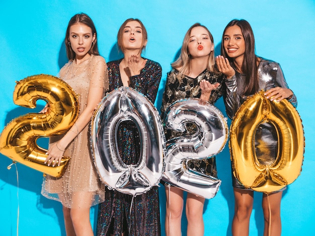 Gelukkige prachtige meisjes in stijlvolle sexy feestjurken met gouden en zilveren 2020-ballonnen