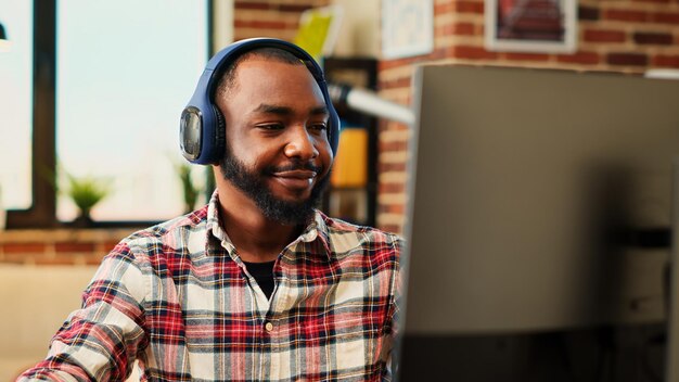 Gelukkige remote werker luistert naar muziek op hoofdtelefoon terwijl hij van thuis werkt Ontspannen glimlachende freelancer geniet van het typen op de computer in een stijlvol appartement persoonlijk kantoor van dichtbij