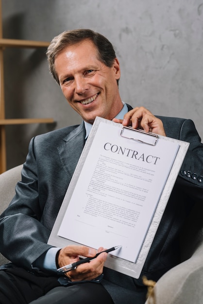 Gelukkige rijpe advocaat die op handtekeningsplaats op een contractdocument richten met pen