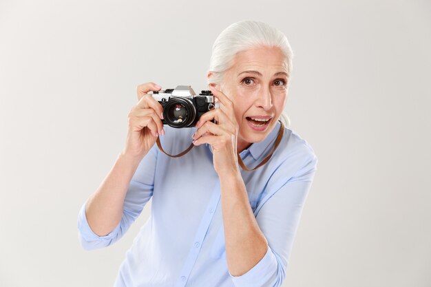 Gelukkige rijpe vrouw die retro camera geïsoleerd houden