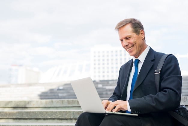 Gelukkige rijpe zakenman die aan laptop bij openlucht werken