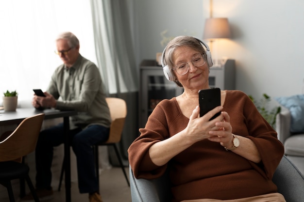 Gelukkige senior vrouw die smartphone gebruikt in de woonkamer van een modern appartement
