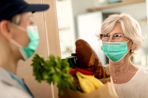 Gelukkige senior vrouw met gezichtsmasker die thuisbezorgd wordt tijdens de coronavirusepidemie