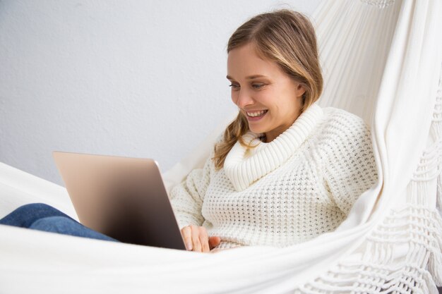 Gelukkige studentenzitting in hangmat en het gebruiken van laptop