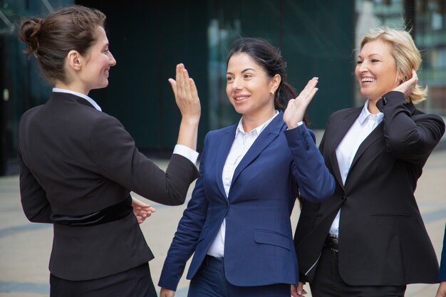 Gelukkige succesvolle bedrijfsdames die high five geven. Onderneemsters die pakken dragen die in stad samenkomen. Teamsucces en teamwerkconcept