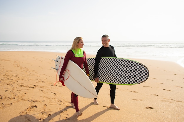 Gelukkige surfers die van strand weggaan en spreken