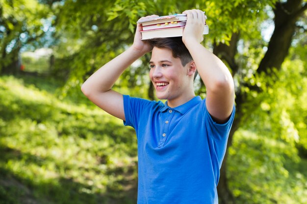 Gelukkige tienerjongen met boeken op hoofd