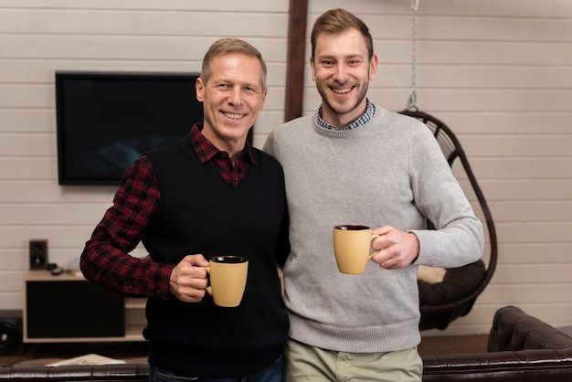 Gratis foto gelukkige vader en zoon die terwijl het houden van koppen stellen