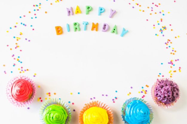 Gelukkige verjaardagstekst met kleurrijke muffins op witte achtergrond