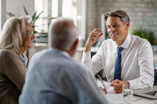 Gelukkige verzekeringsagent die met een volwassen stel praat over hun pensioenplannen tijdens de vergadering op kantoor