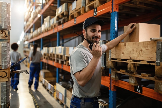 Gelukkige verzender die walkietalkie gebruikt tijdens het werken in het distributiemagazijn