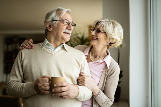 Gelukkige volwassen man en vrouw communiceren terwijl ze thuis bij het raam staan