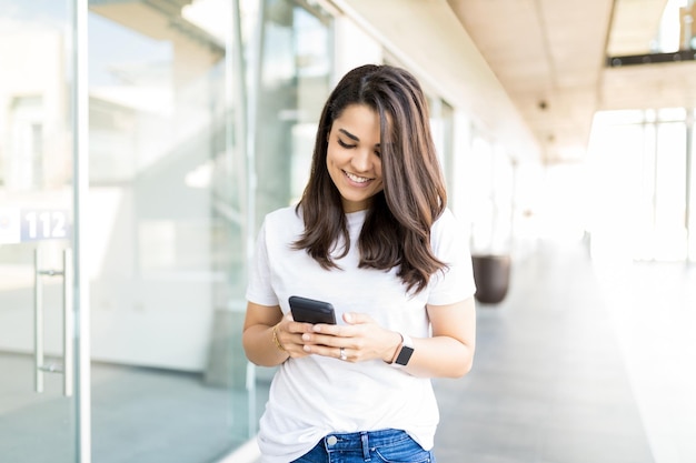 Gelukkige volwassen vrouw die inkomende melding op smartphone in winkelcentrum leest