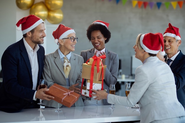 Gelukkige volwassen zakenvrouw krijgt een cadeau van haar collega's op kerstfeest op kantoor