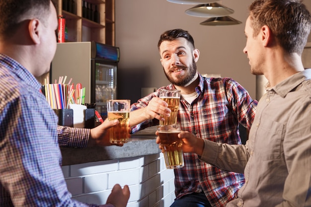 Gratis foto gelukkige vrienden die bier drinken bij teller in bar