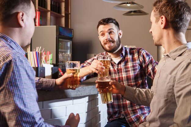 Gelukkige vrienden die bier drinken bij teller in bar