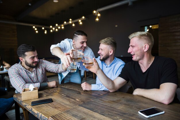 Gelukkige vrienden die met whiskyglazen in de bar toejuichen