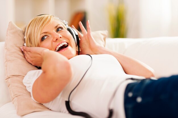 Gelukkige vrouw die aan muziek op bank luistert