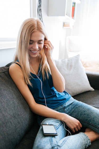 Gelukkige vrouw die aan muziek van mobiele telefoon thuis luistert