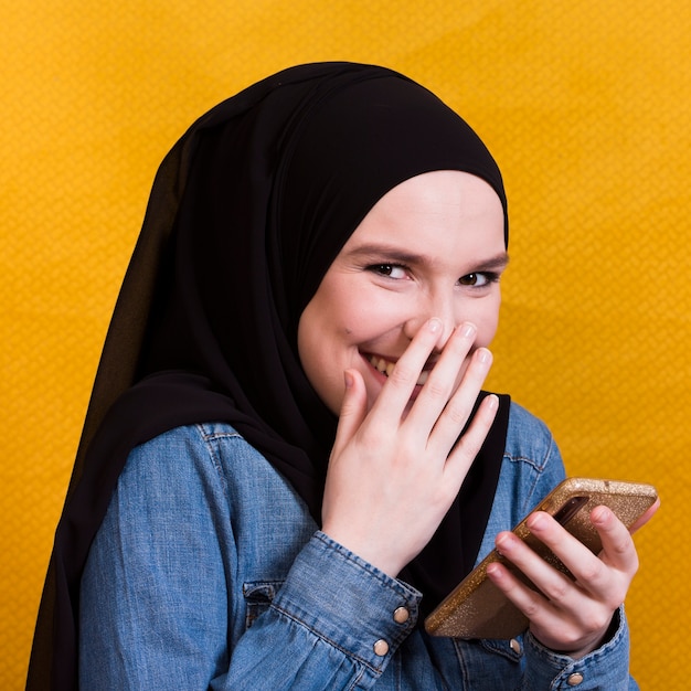 Gelukkige vrouw die denimoverhemd dragen die smartphone op heldere achtergrond gebruiken
