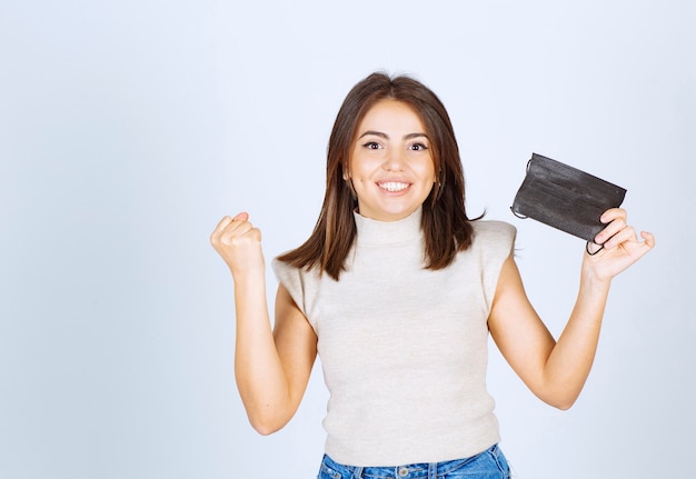 Gelukkige vrouw die een zwart medisch masker houdt en glimlacht.