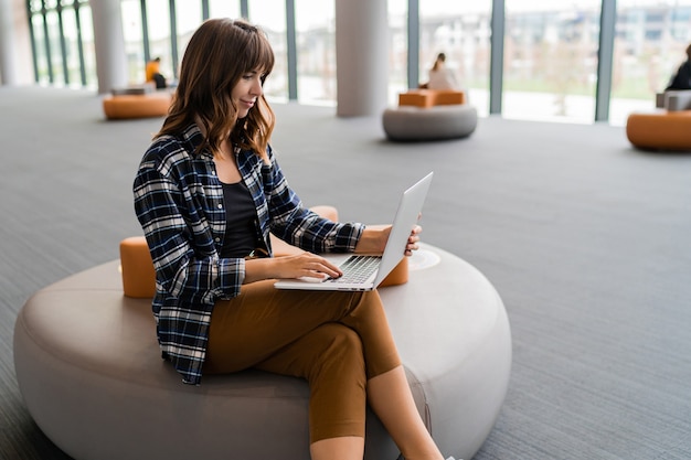 Gelukkige vrouw die lap top gebruikt terwijl zittend in de luchthavenlounge.