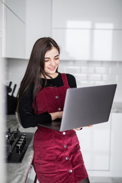 Gelukkige vrouw die laptop thuis in de keuken met behulp van