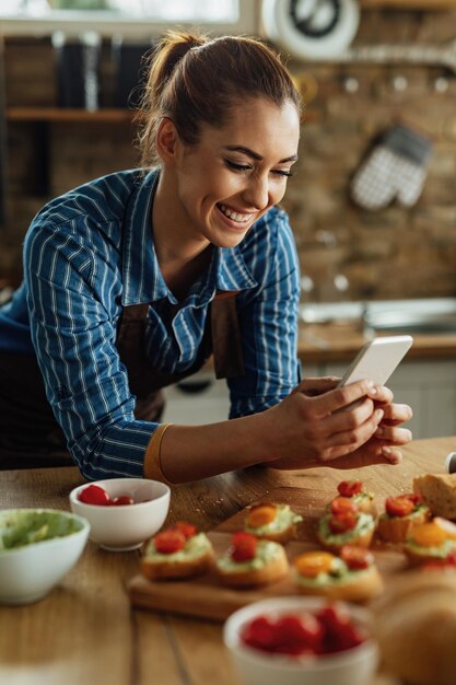 Gelukkige vrouw die smartphone gebruikt en voedsel fotografeert dat ze in de keuken heeft bereid