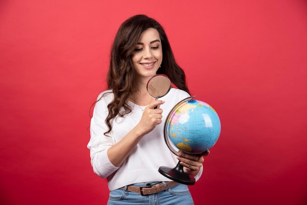 Gelukkige vrouw die wereldbol met vergrootglas bekijkt. Hoge kwaliteit foto