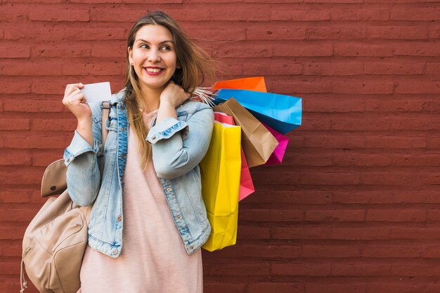 Gelukkige vrouw die zich met het winkelen zakken en creditcard bij rode bakstenen muur bevinden